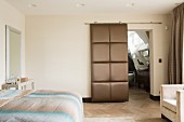 Double bed and open, upholstered sliding door leading to ensuite bathroom in bedroom