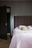 Bedspread on bed with tall, button-tufted headboard against wallpapered wall