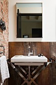 Washstand with chrome frame against rusty, Corten steel wall and below mirror in corner of bathroom