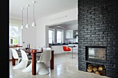 Offener, moderner Wohnraum mit Retro Flair - weiße Klassiker Schalenstühle um Esstisch, seitlich Kamin in schwarz gestrichener Ziegelwand