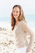 A happy young woman on a beach wearing a crocheted jumper