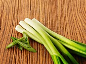 Spring onions, partially sliced, on a wooden surface