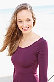 A happy young woman by the sea wearing a long-sleeved, purple dress