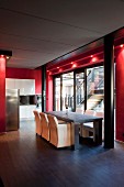 Dining area and kitchen in open-plan interior with glass wall framed in red