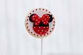 A round biscuit lolly decorated with a red bow and dots
