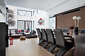 Futuristic chairs at long dining table in open-plan, contemporary interior with lounge area in background