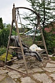 Antike Gartenschaukel mit Tierfell und Zierkissen auf Terrasseplatz mit alten, bemoosten Polygonalplatten