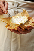 A man holding goat's cheese and a cheese knife