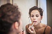 A young woman applying lip gloss in a bathroom mirror