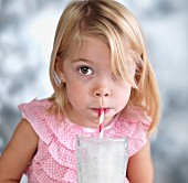 A blonde girl blowing bubbles through a straw into a glass of milk