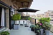 Planters and open parasol above seating area on terrace of penthouse apartment with view across city