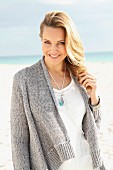 A blonde woman on a beach wearing a white blouse and a grey cardigan