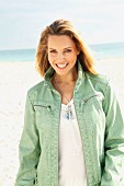 Blonde Frau in weisser Bluse und grüner Lederjacke am Strand