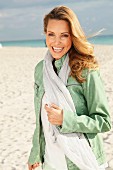 Blonde Frau in weisser Bluse, grüner Lederjacke und mit Schal am Strand
