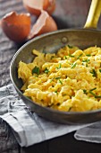 Scrambled eggs with chives in a pan on a wooden surface