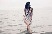 Frau im Sommerkleid läuft am Strand durchs Wasser