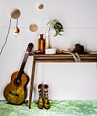 Gitarre an Konsolentisch aus Holz, dekoriert mit Vintage Flasche, Netztasche und Hut, auf Boden projiziertes Naturmotiv