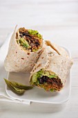 A burrito filled with beans, beef, guacamole, lettuce and tomato rice