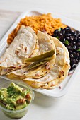 Quesadillas filled with cheese served with black beans, tomato rice and guacamole