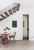 Table and chairs under staircase and sliding door with view into narrow corridor in modern foyer