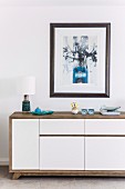 Sideboard with wooden casing and white-painted doors under framed picture on wall