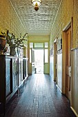 Antique sideboard on wooden floor and walls and ceiling covered in ornamental metal tiles in long narrow hallway