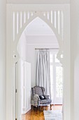 White-painted ogee arch built into doorway and view of comfortable armchair in front of French windows