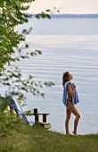 Frau mit Badekleidung und Handtuch vor ruhig liegendem See