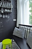 Black bench with scatter cushions and neon yellow stool against chalkboard wall