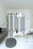 Grey knitted pouffe next to white side table in front of white wardrobe with glass door panels