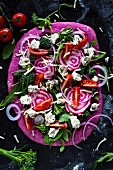 Beetroot pizza dough with broccolini, red onions, tomatoes, goat's cheese, rocket and cheese (unbaked)