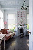 Antique couch next to windows with roller blinds, black wood-burner, wooden ceiling and black wooden floor in rustic interior