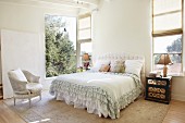 Helles Schlafzimmer mit Doppelbett und Rüschen Tagesdecke, seitlich offenes Fenster mit Gartenblick