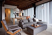 Loungebereich mit grauem Sofa und passendem Polster-Couchtisch, dahinter Essplatz in eleganter Loftwohnung