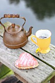 A cup of tea and a heart-shaped doughnut on the bank of a lake