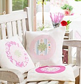 Hand-sewn scatter cushions with various patterns and appliqué motifs on wooden garden chair