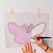 Zart lilafarbene Schablonenmalerei an Wand - Selbstgemachte Schmetterling-Schablone mit Frauenhänden und Malpinsel