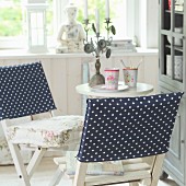 Hand-sewn, dark blue loose covers with white polka dots on two white, wooden folding chairs