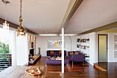 Offener, moderner Wohnraum mit sichtbarer Tragwerkkonstruktion, im Hintergrund Loungebereich mit violetter Sofagarnitur