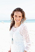 A young, long-haired woman on a beach wearing a white lace dress