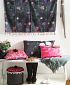Cushions with hand-sewn covers in ethnic, hippy style on wooden bench below wall hanging