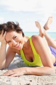 A woman with short, brown hair lying on a sandy beach wearing a sports bra and shorts