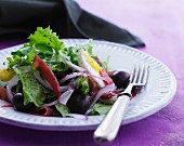 A mixed leaf salad with olives, ham and egg