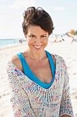 A woman with short, brown hair on the beach wearing a light knitted jumper