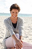 A woman with short brown hair by the sea wearing a grey jumper
