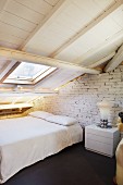 Purist bedroom under sloping attic roof with white-painted wooden structure; retro lamp on bedside table and partial view of vintage figure to one side