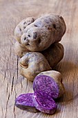 Purple potatoes, whole and halved, on a wooden surface