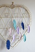 Colourful, modelling compound feathers hanging from wire heart as wall decoration