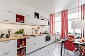 A renovated living-kitchen area with white cupboards, red-and-white striped curtains and a dining area