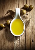 Ein Löffel Olivenöl und grüne Oliven auf Holzuntergrund